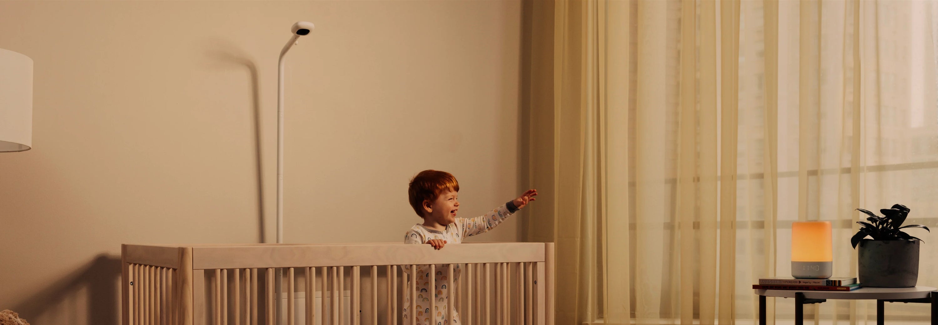 Baby smiling inside the crib while looking at sound + light and pro camera with floor stand looking down at crib